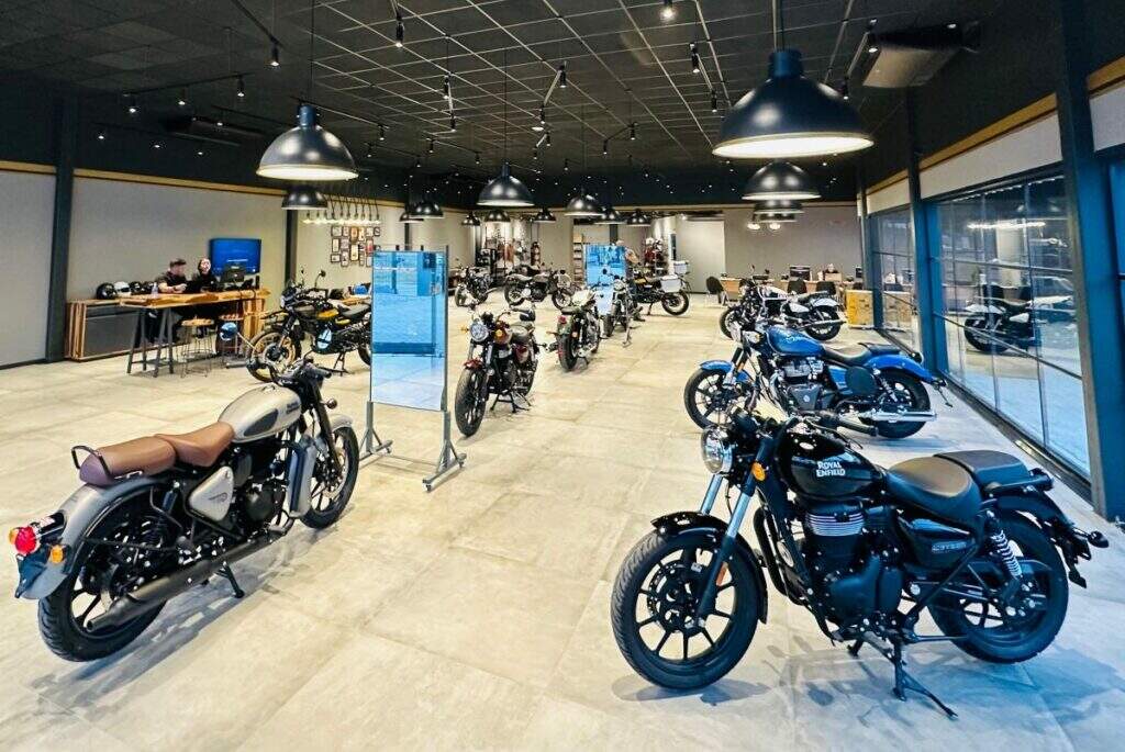 Uma vista interna da nova concessionária Royal Enfield em Duque de Caxias, mostrando diversas motocicletas expostas no showroom espaçoso e bem iluminado. Ao fundo, é possível ver uma área de atendimento com mesas e cadeiras.