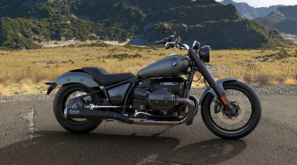 Motocicleta BMW R18 Blacked Out vista de lado, com a maior parte do veículo em preto fosco, incluindo o tanque de combustível, o motor grande e os escapamentos. Há alguns detalhes cromados e o logotipo da BMW no motor.
